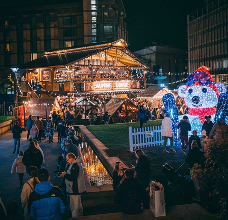 An Alpine Lodge, lit up with fairy lights, sits in the middle of the Peace Gardens as part of the Sheffield Christmas Market. In the foreground is a huge light-up polar bear.
