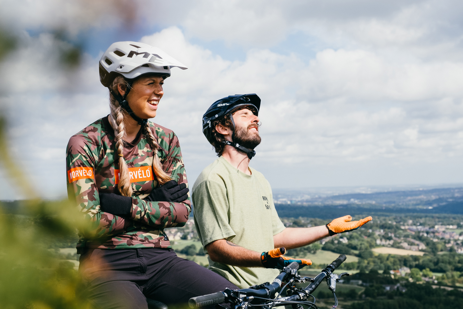 Female and male cyclists taking a break on their bikes, whilst looking out to Sheffield on a sunny day.