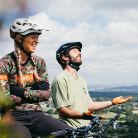 Female and male cyclists taking a break on their bikes, whilst looking out to Sheffield on a sunny day.