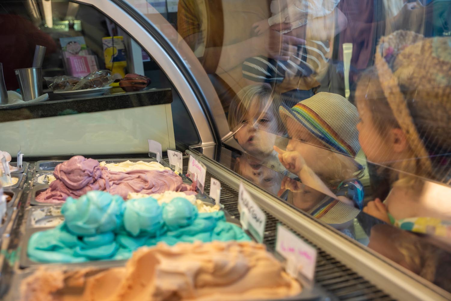 Children leaning on a glass counter looking at all the different flavours of ice cream.
