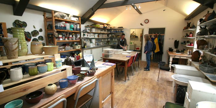 An artists studio with a huge work table and lots of shelves filled with art materials. 