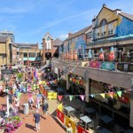 Orchard Square in the sunshine decorated with bunting. There are lots of people walking about.