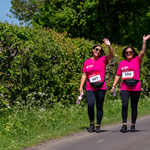 Two women, both wearing pink t-shirts, are walking down a lane on a sunny day.