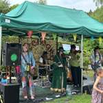 A band playing live in a park, under a pop-up gazebo. 