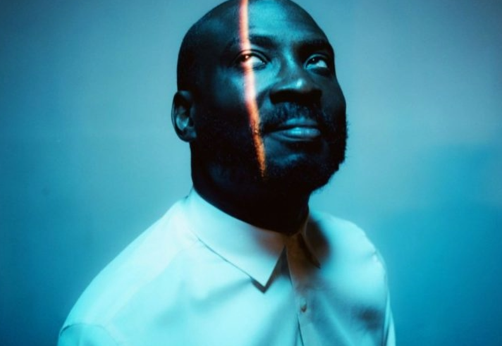 Joshua Idehen, looking upwards, in subdued blue lighting.