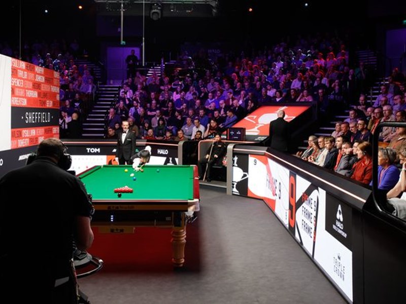 A snooker table is set up and a crowd waits for the frame to start.