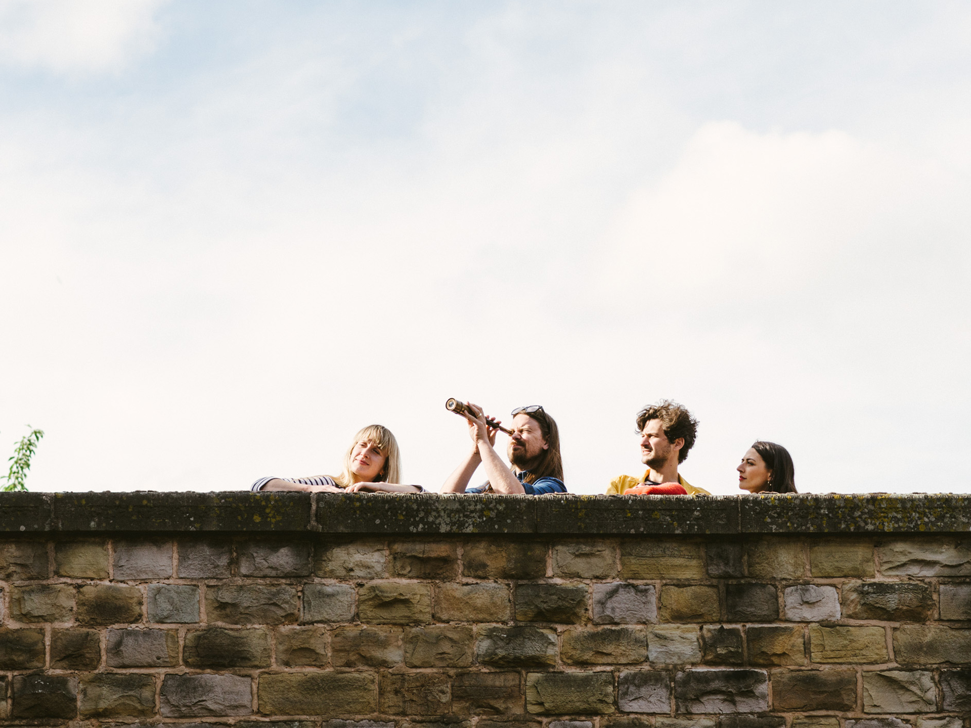 Four people looking over a high wall, one with a telescope, playing Treasure Hunt Sheffield.