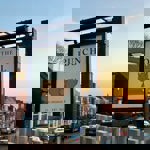 A hanging pub sign for The Punch Bowl in Crookes, featuring a stylised punch bowl illustration, photographed at sunset with rows of terraced houses in the background.