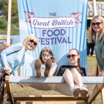 Two children sitting on a giant deck chair that has the Great British Food Festival logo on the backrest. 