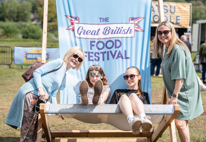 Two children sitting on a giant deck chair that has the Great British Food Festival logo on the backrest. 