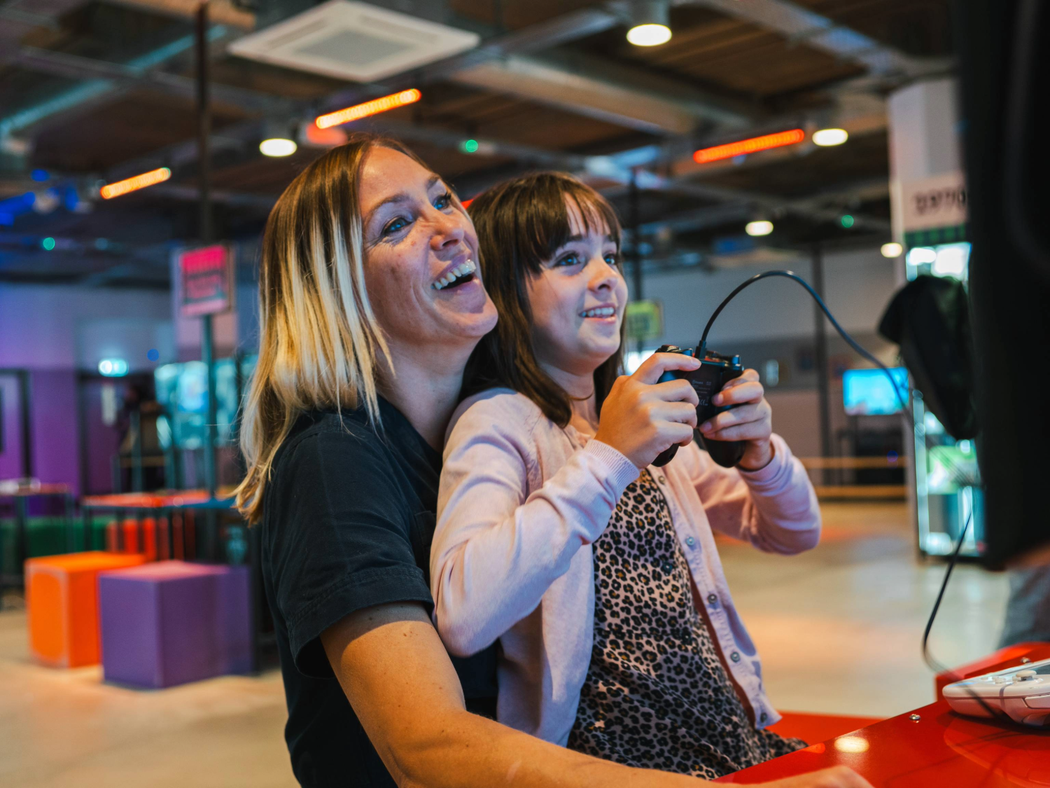 A person with a child sat on their knee are playing a video game together. In the background are displays of video games from the history of the video game industry.