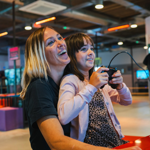 A person with a child sat on their knee are playing a video game together. In the background are displays of video games from the history of the video game industry.