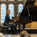 A person playing a grand piano, on a stage, in front of an audience.