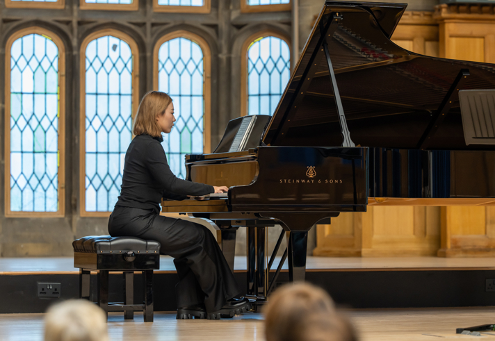 A person playing a grand piano, on a stage, in front of an audience.