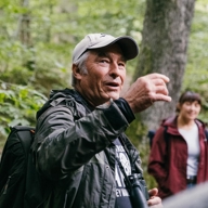 Man talking whilst walking in the woods. A man and woman from the same group can be seen in the background.