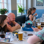 Two tables at The Treehouse Cafe, both filled with people enjoying drinks and playing board games.