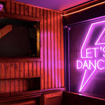 A pink neon sign with a lighting bolt and the words 'Let's Dance'.