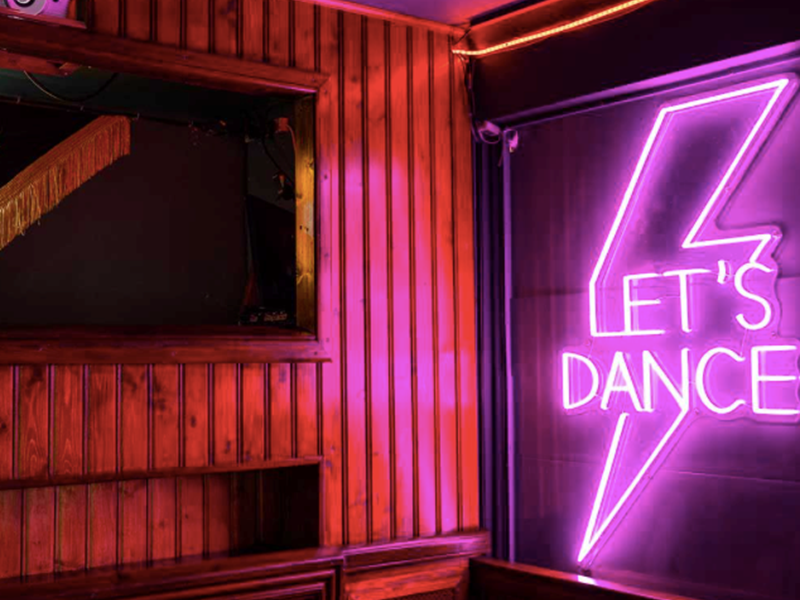 A pink neon sign with a lighting bolt and the words 'Let's Dance'.