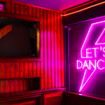 A pink neon sign with a lighting bolt and the words 'Let's Dance'.