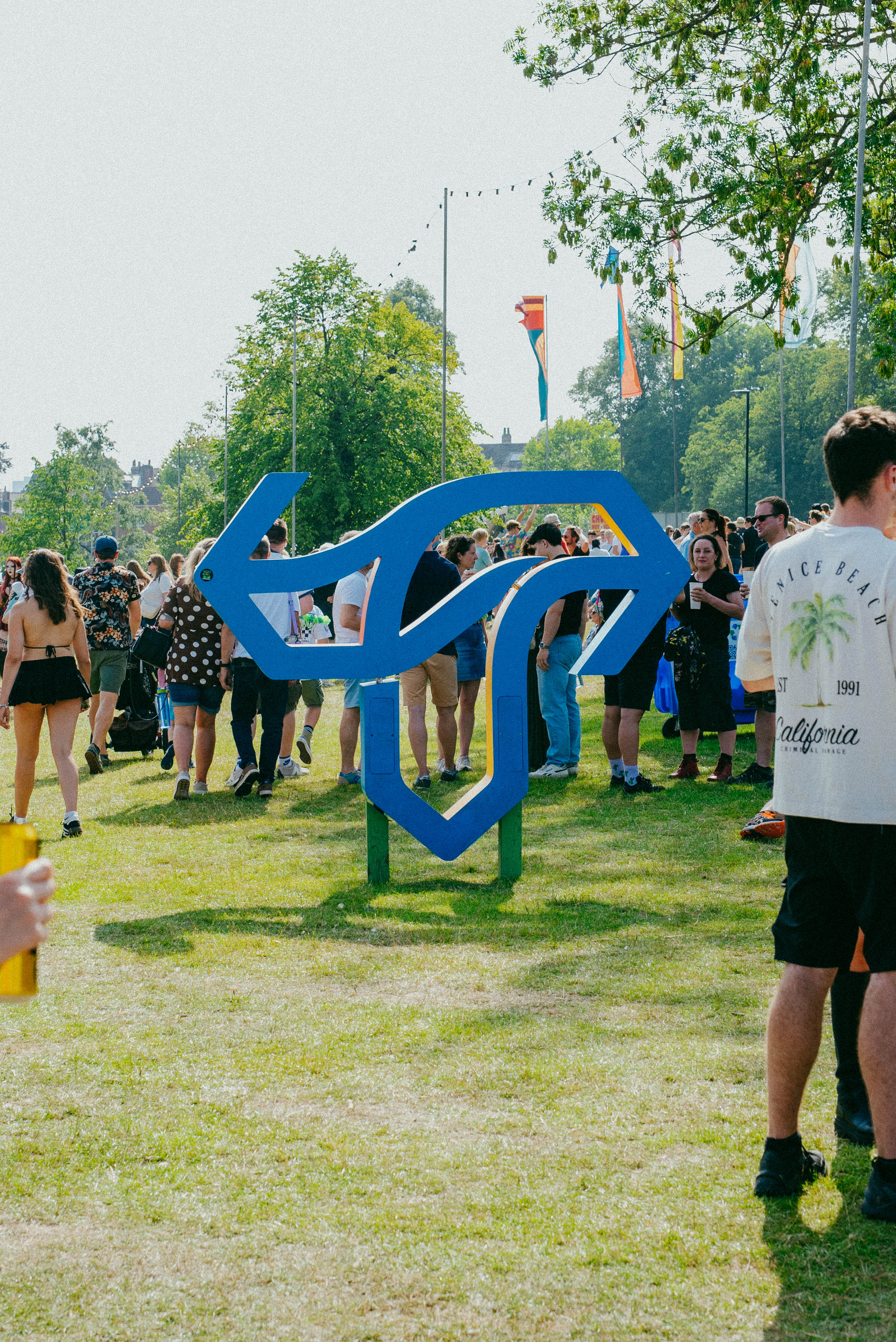 A giant sculpture of the Tramlines festival logo stands on the grass as a crowds of festivalgoers walk by 