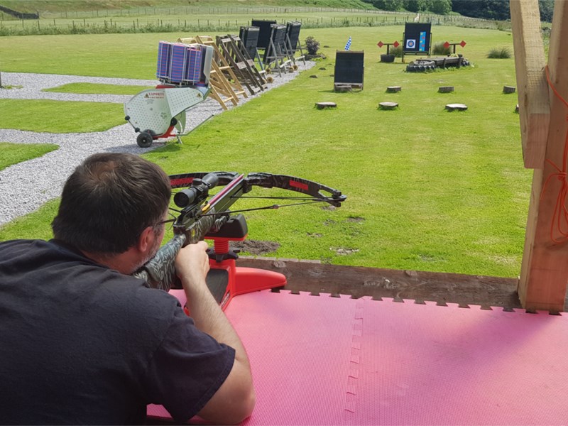 A person firing a crossbow at a target on a shooting range.
