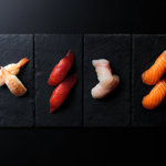 An overhead shot of four portions on sushi artfully arranged on pieces of slate.