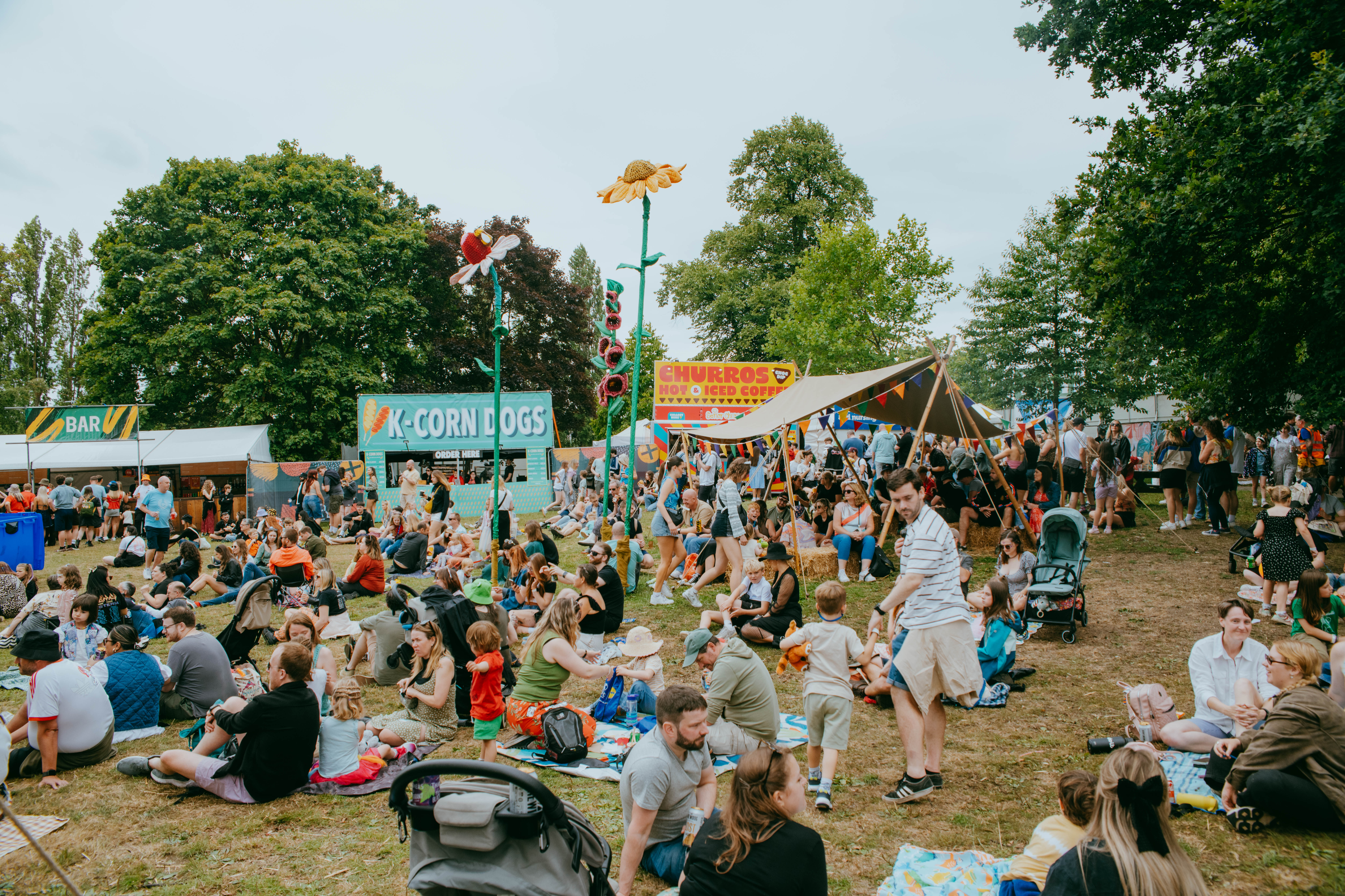 Families sit out on picnic blankets eating as other people queue for food from street food stalls at Tramlines festival 