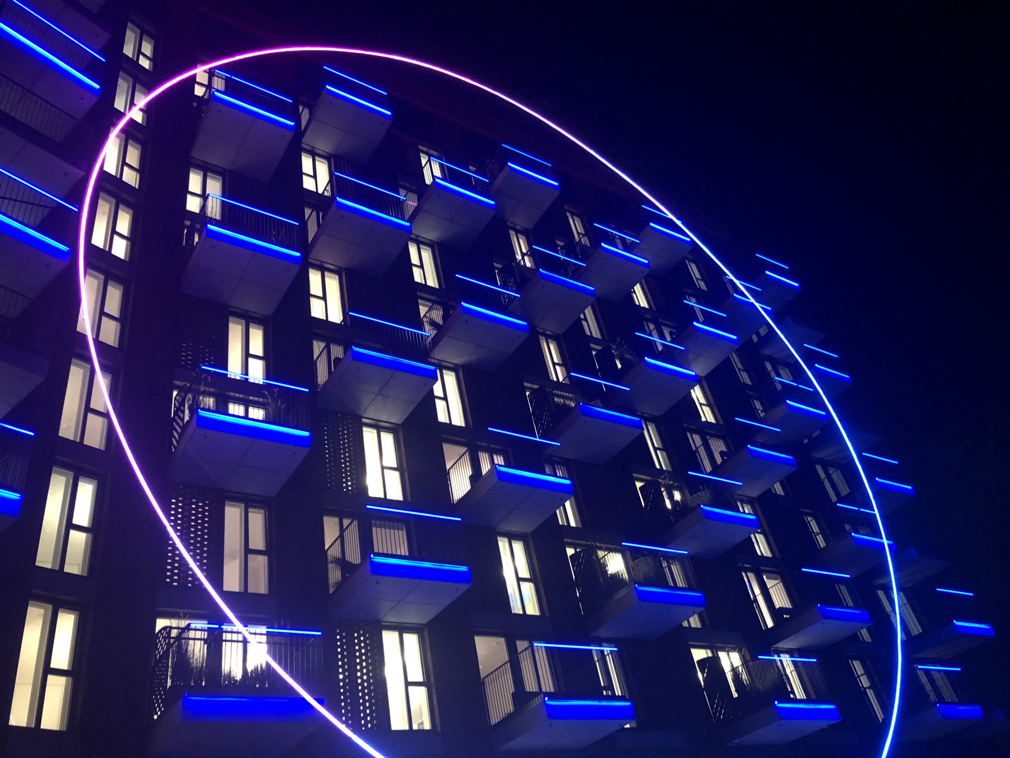 An exterior shot of the Joi Polloi building, at night, lit up by moody blue lighting.