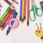 A white surface covered in arts supplies including coloured pencils, crayons and paints.