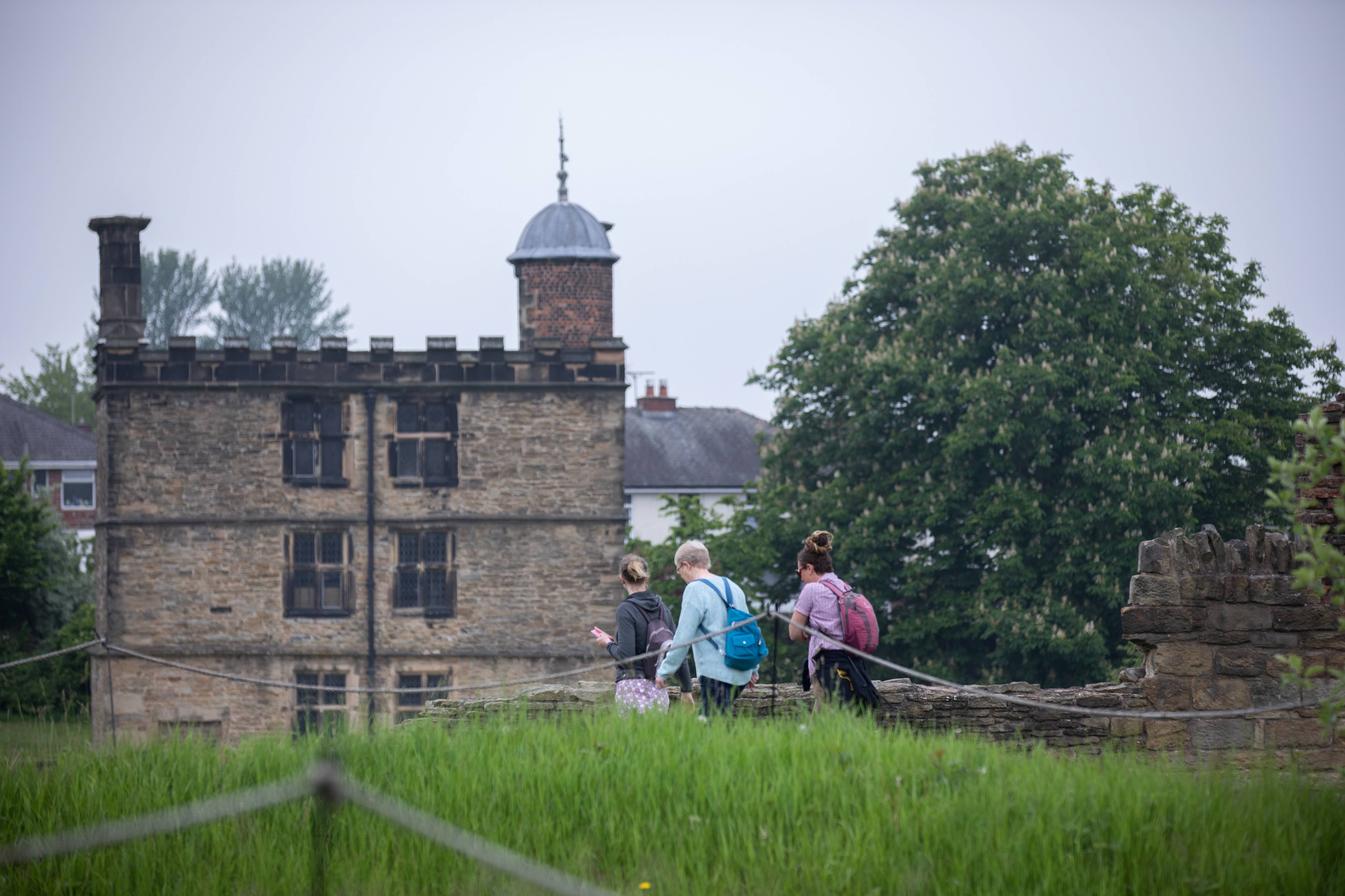 Three people with rucksacks are walking towards Sheffield Manor Lodge.