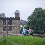Three people with rucksacks are walking towards Sheffield Manor Lodge.
