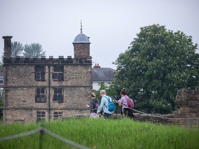 Three people with rucksacks are walking towards Sheffield Manor Lodge.