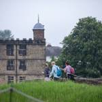 Three people with rucksacks are walking towards Sheffield Manor Lodge.