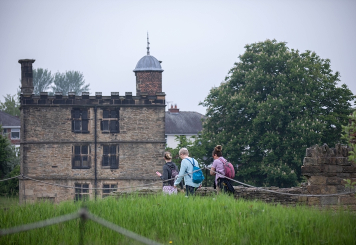 Three people with rucksacks are walking towards Sheffield Manor Lodge.