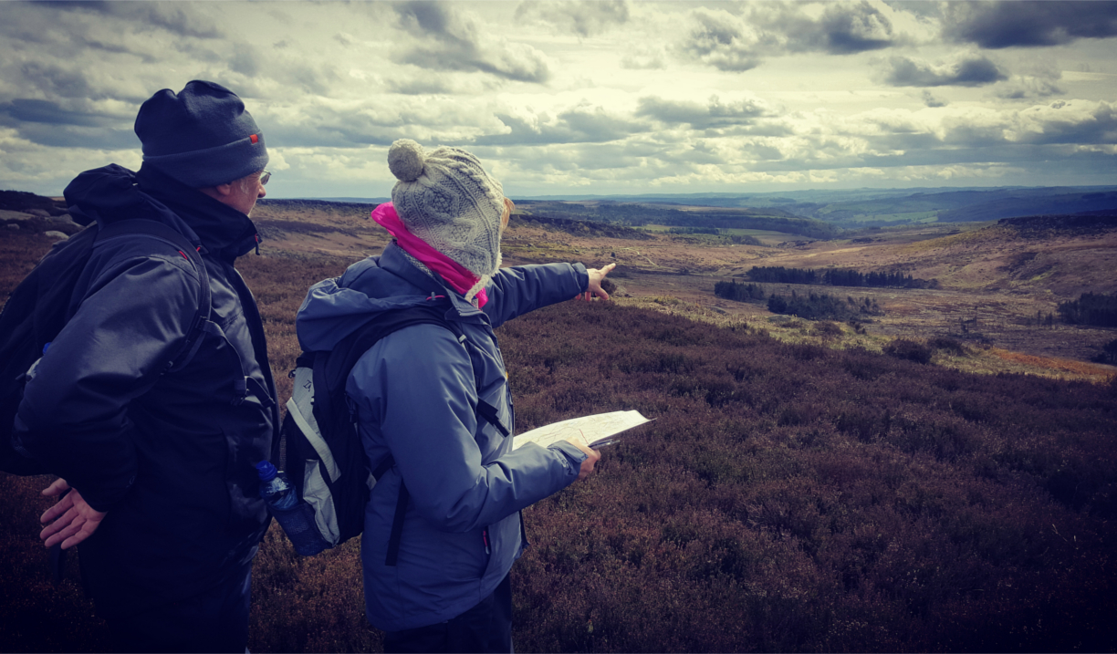 Two people out walking in the countryside, one of them is holding an open map.