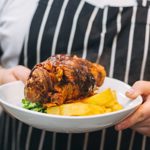 A man in a blue and white striped apron carries a plate of food.
