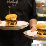 A woman carries two plates, each with a breakfast muffin on.