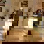 Reception desk in the Leopold Hotel - Reception area of a hotel with a modern glass-front desk illuminated by soft lights. Behind the desk are framed certificates and a tall floral arrangement. The space features cream-colored walls, arched doorways, and tiled flooring. A wooden bench is positioned along the left wall, and an open doorway in the background reveals a decorative sculpture on a shelf.