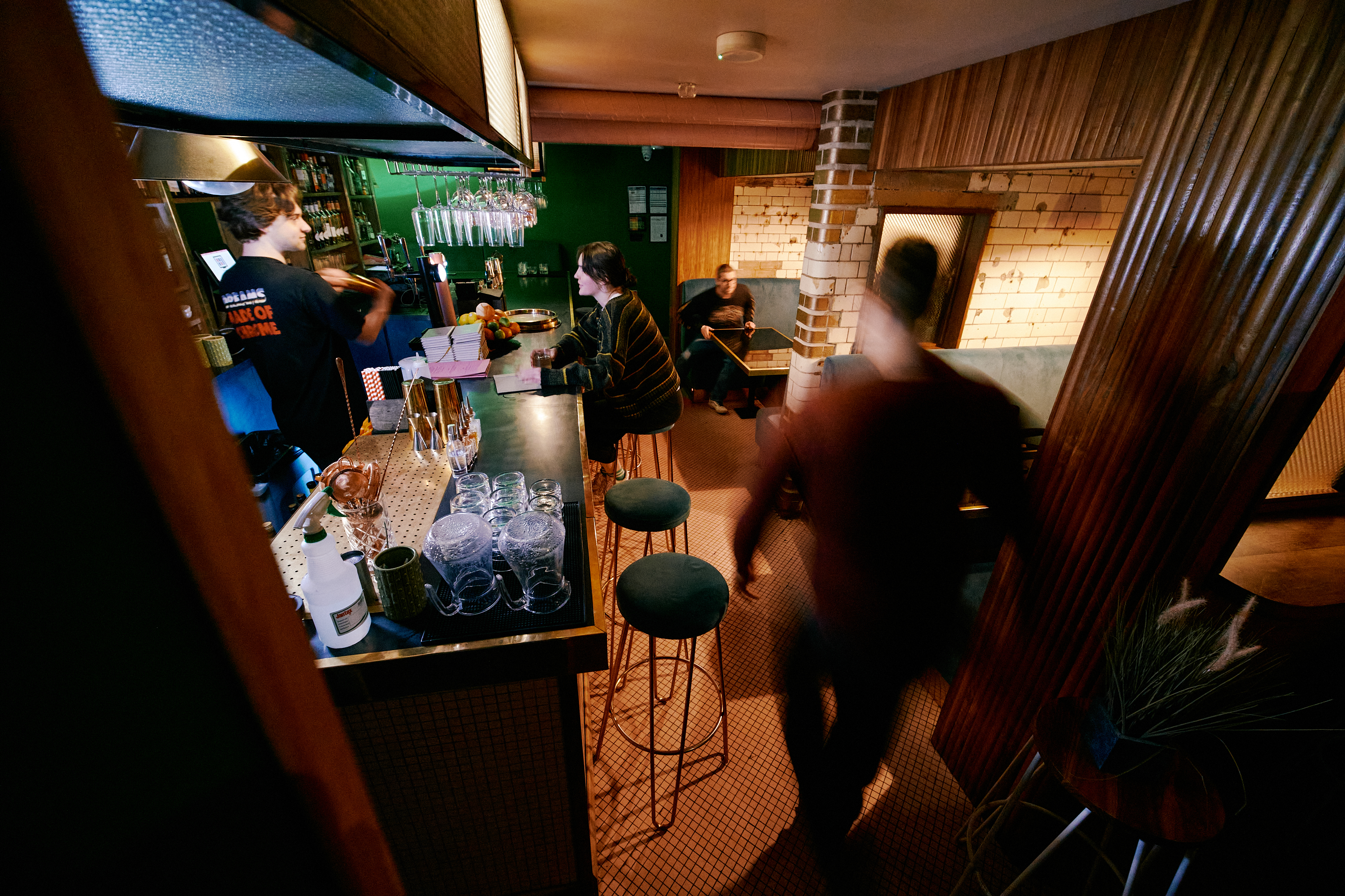 Interior shot of Public, a cocktail bar in the centre of Sheffield. There are people sat in booths and at the bar, where a barman is serving drinks.