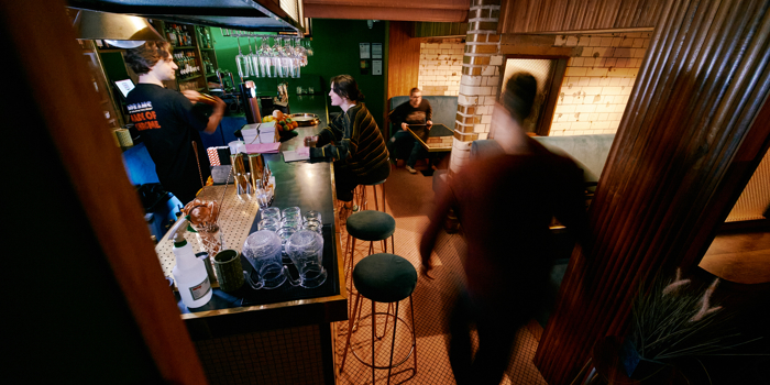 Interior shot of Public, a cocktail bar in the centre of Sheffield. There are people sat in booths and at the bar, where a barman is serving drinks.