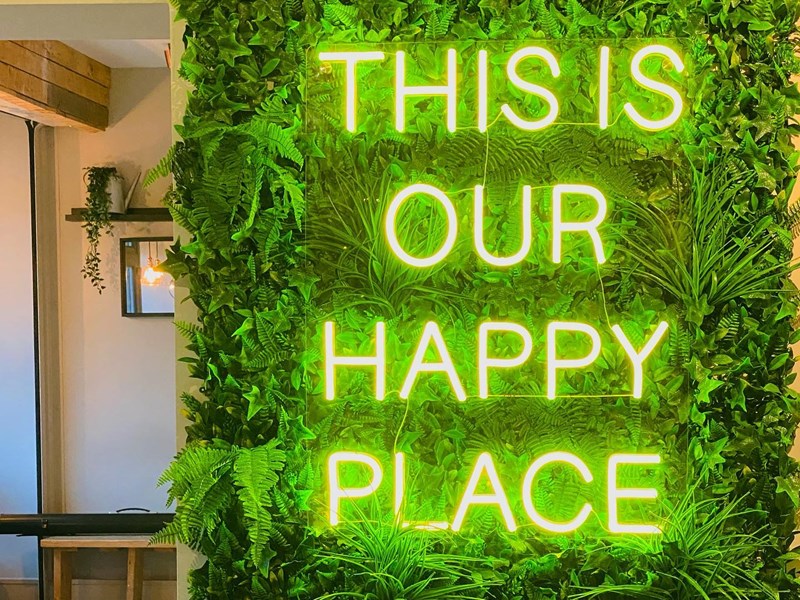 A green neon sign that reads 'This is our happy place' on the wall at S17 Coffee Shop & Bistro.