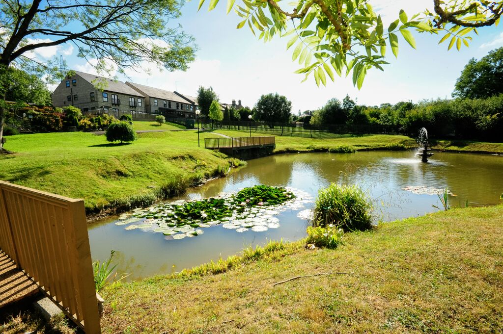 A pond with a footbridge spanning it, with a building in the background.