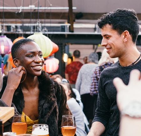 A woman and a man are sat chatting and having a drink in a bar.