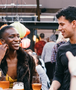 A woman and a man are sat chatting and having a drink in a bar.