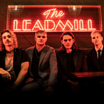 A picture of the band which consists of 4 people sitting on a sofa and above them is a neon sign of The Leadmill