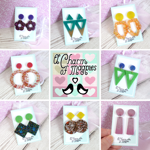 Nine-image grid showcasing colorful handmade geometric earrings in various shapes and finishes, including glitter circles, green triangles, yellow and orange hoops, and pink rectangles, with central logo reading 'A Charm of Magpies' surrounded by pastel hearts.