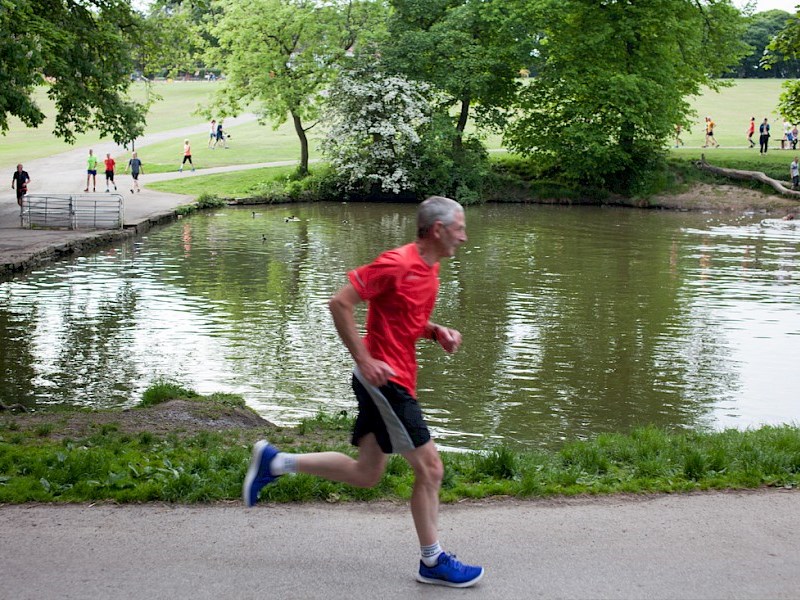 A man running on a path that goes around one of the ponds at Graves Park.