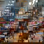  A warm, vintage‑style pub dining area with patterned wallpaper, red leather booth seating, wooden tables, and a lit fireplace beneath a decorative mirror.