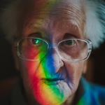 A close-up portrait senior woman with rainbow face wearing spectacles.
