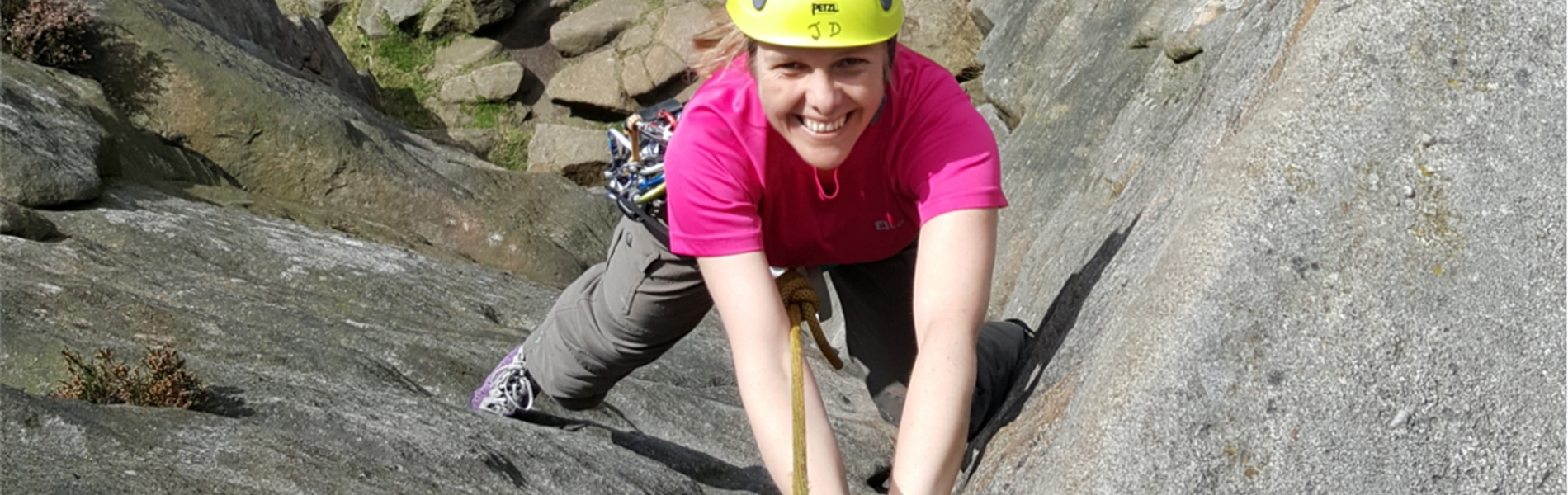 A woman climbing a rock face with a big smile on her face.